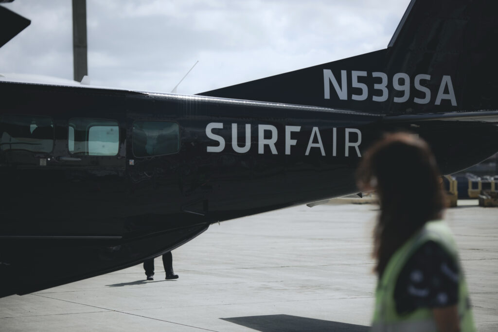 Ramp agent walking past a Surf Air Cessna Grand Caravan EX on the apron